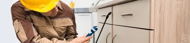 Roach exterminator applying treatment under kitchen cabinets in Rockford, IL